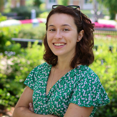 Portrait of Camille Boucaud. She is standing in a garden and smiling at the camera. 