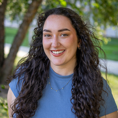 Grace Semaan smiles at the camera. She is standing outside and is wearing a blue shirt.