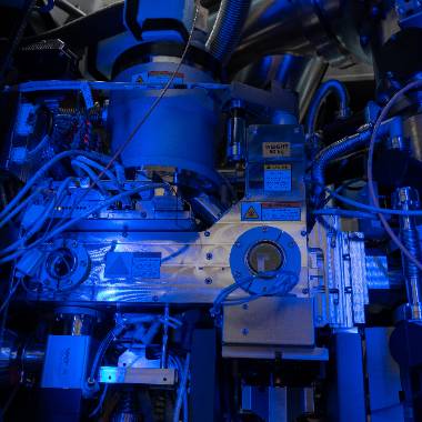 A Cryo-EM machine glows blue and silver in a dark room. 