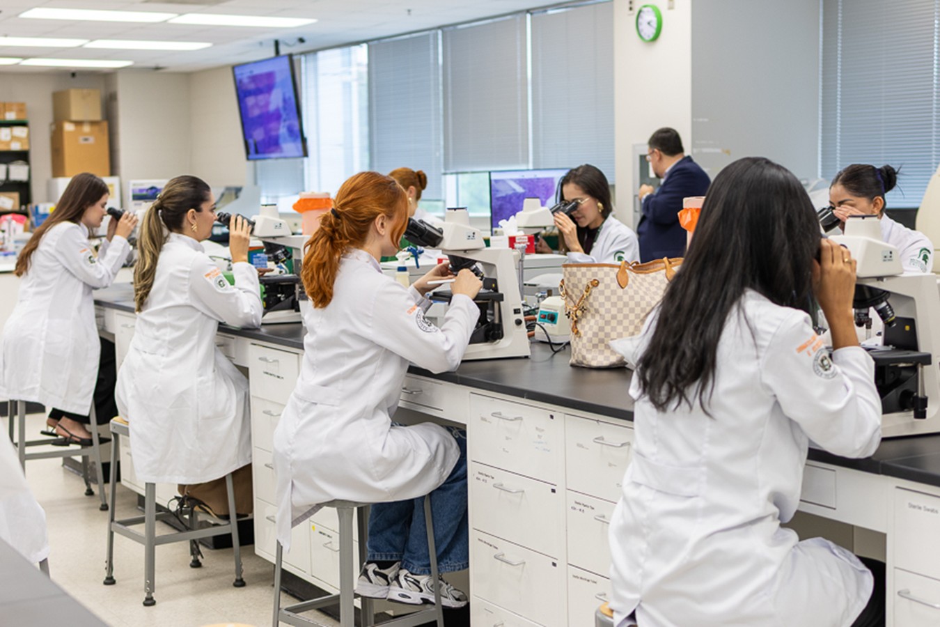 A group of students wearing lab coats looks through microscopes.