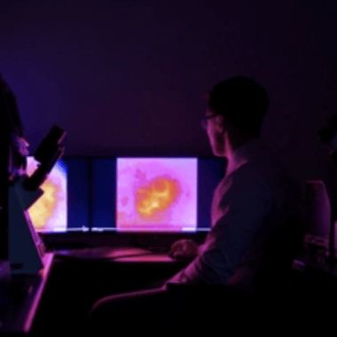 A person in a dark room looks at a screen that has a hot pink and orange image in the shape of a heart.