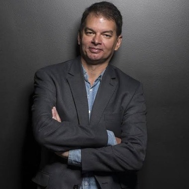 Picture of Chris Adami with his arms crossed looking at the camera. He is leaning against a gray wall.