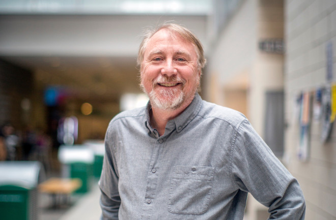 White man with brown hair and beard wearing blue collared shirt is the lobby of a building.