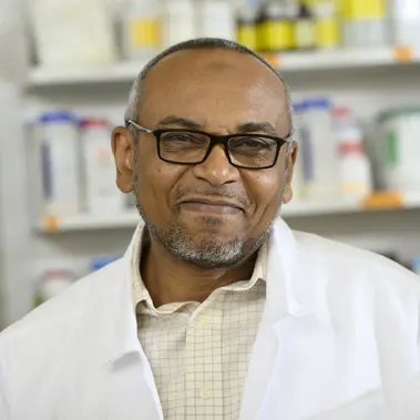 Dr. Mohamed Satti smiles at the camera. He is in a lab and is wearing a lab coat. 