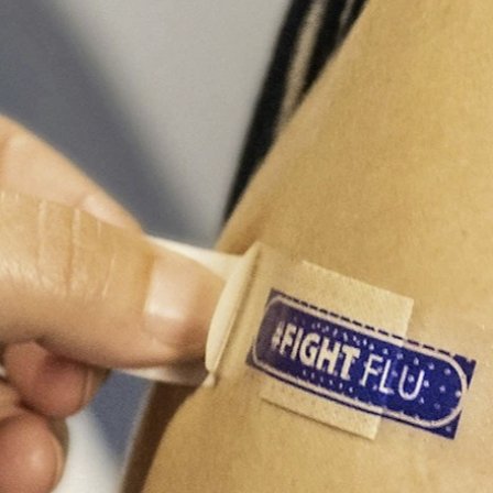 A hand is seen putting a band aid on someone's arm. The band reads 