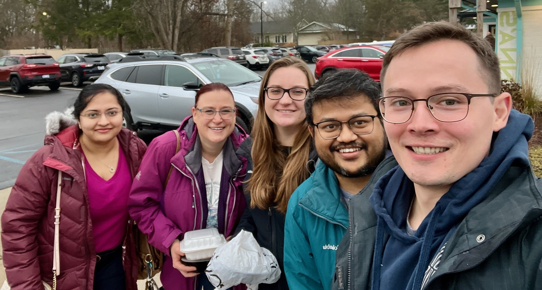 A group of five people take a selfie together. They are wearing winter coats.