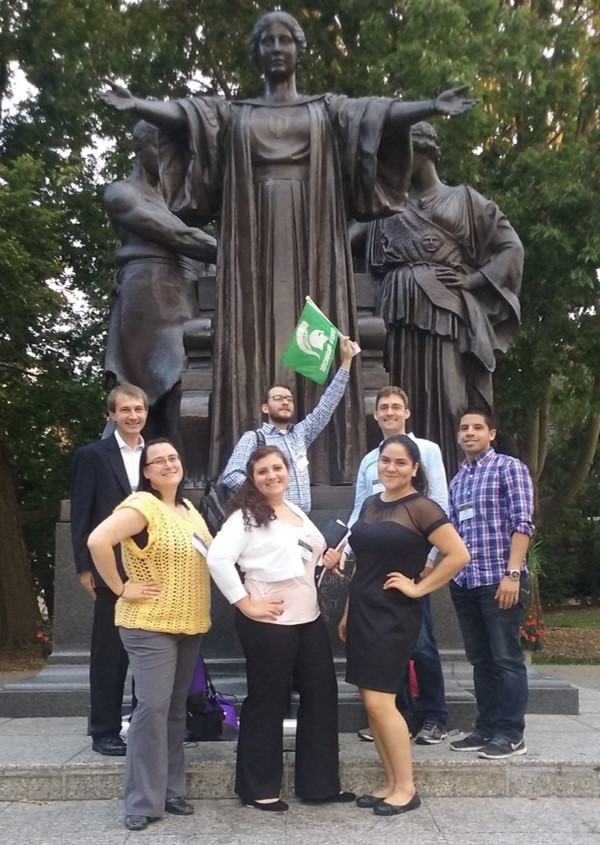 A group of people strike a pose underneath a sculpture.