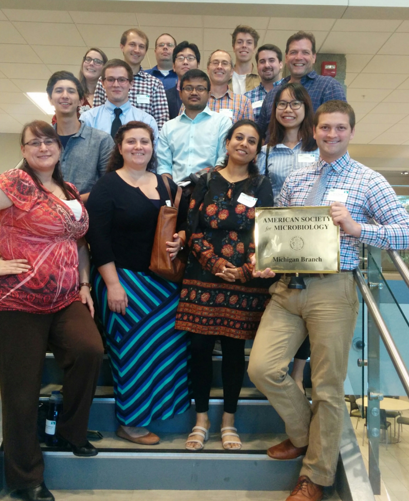 A group of people stand on a staircase. One of them is holding an award of some kind.